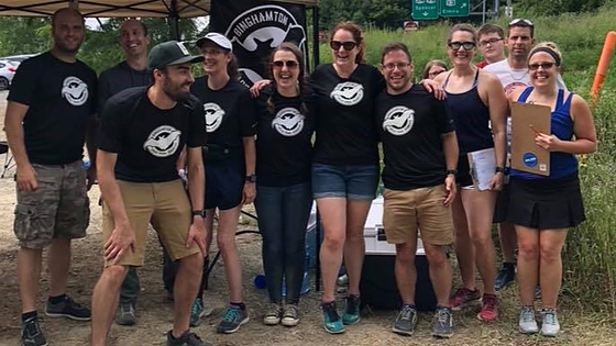 Group photo of the Binghamton Area Trail Runners (BATs) at the Cayuga Trails 50 Miler & Marathon, posing at their aid station surrounded by forest scenery.