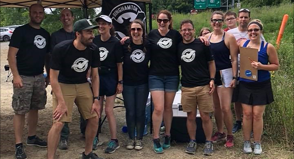 Group photo of the Binghamton Area Trail Runners (BATs) at the Cayuga Trails 50 Miler & Marathon, posing at their aid station surrounded by forest scenery.