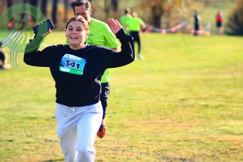Close-up of a runner crossing the STXC Marathon Invitational finish line with arms raised in victory and spectators cheering.