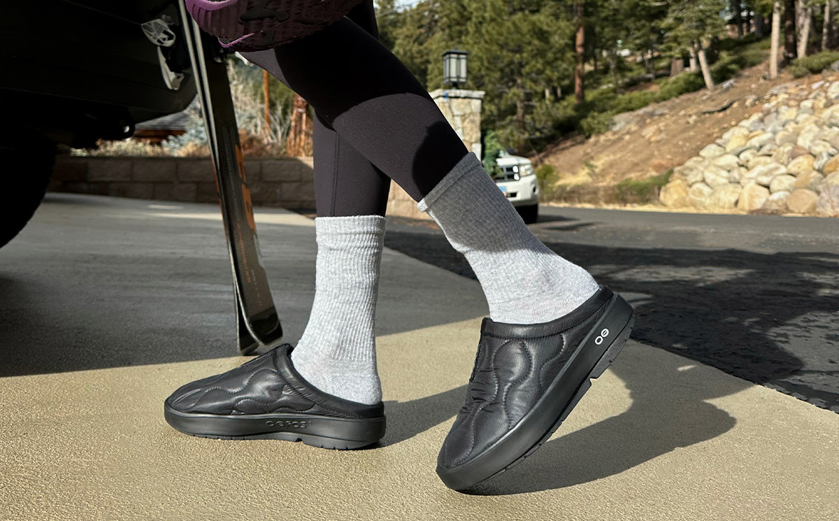 Woman wearing OOFOS OOcoozie Thermo Mule in Black outdoors
