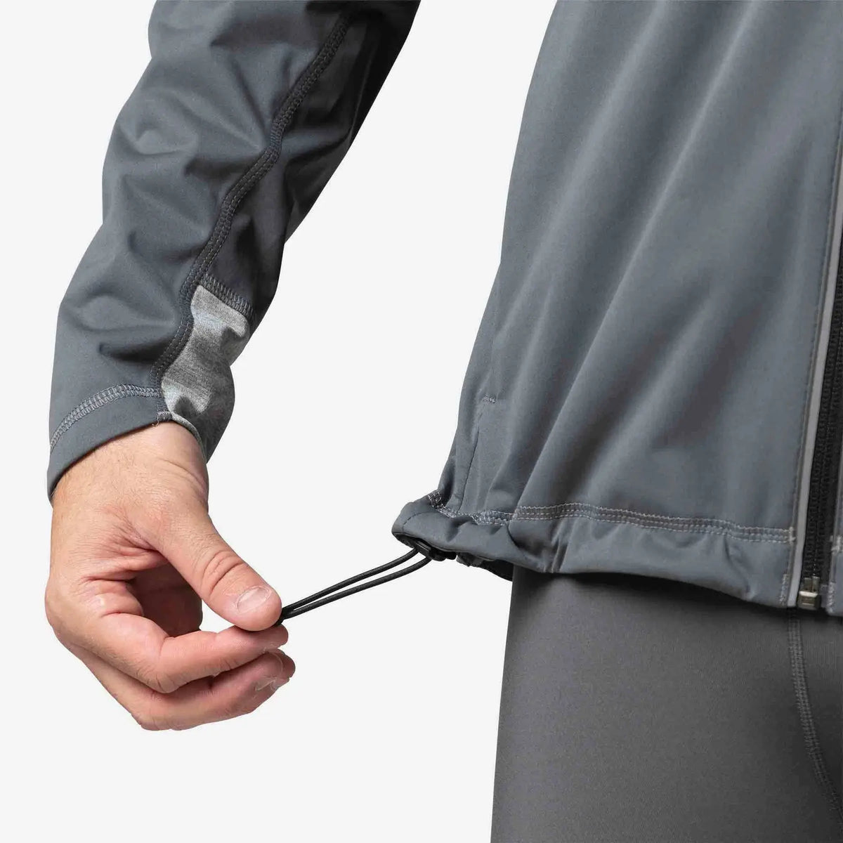 Person adjusting the drawstring of a gray jacket on a white background