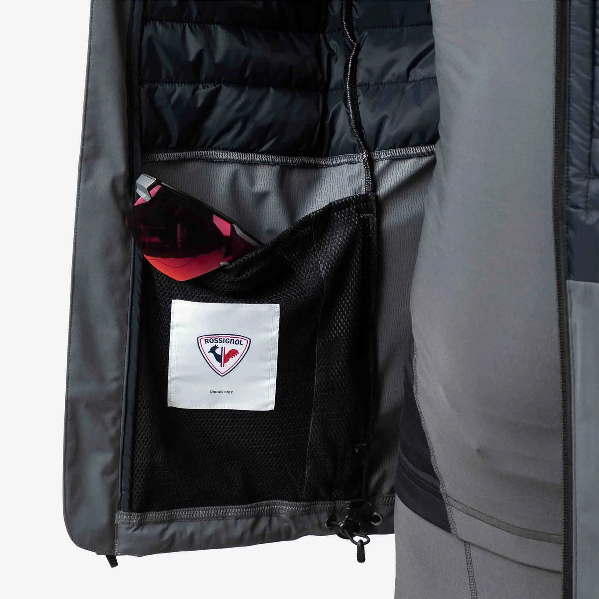 Close-up of a jacket with a pocket containing a red object and a visible brand label on a gray background.