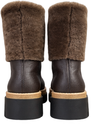 A pair of brown shearling cuffed boots with dark brown pebbled leather shafts and chunky black soles, shown from the back against a white background.