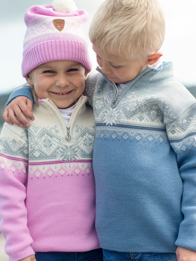 Two children, one in a pink hat and the other in a blue and white sweater, smiling and standing close to each other.