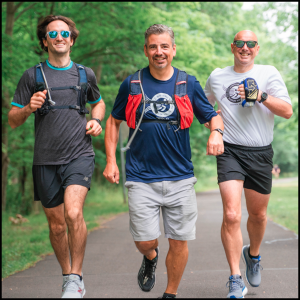 3 male runners decked out for a long run with water bottles and hydration packs.