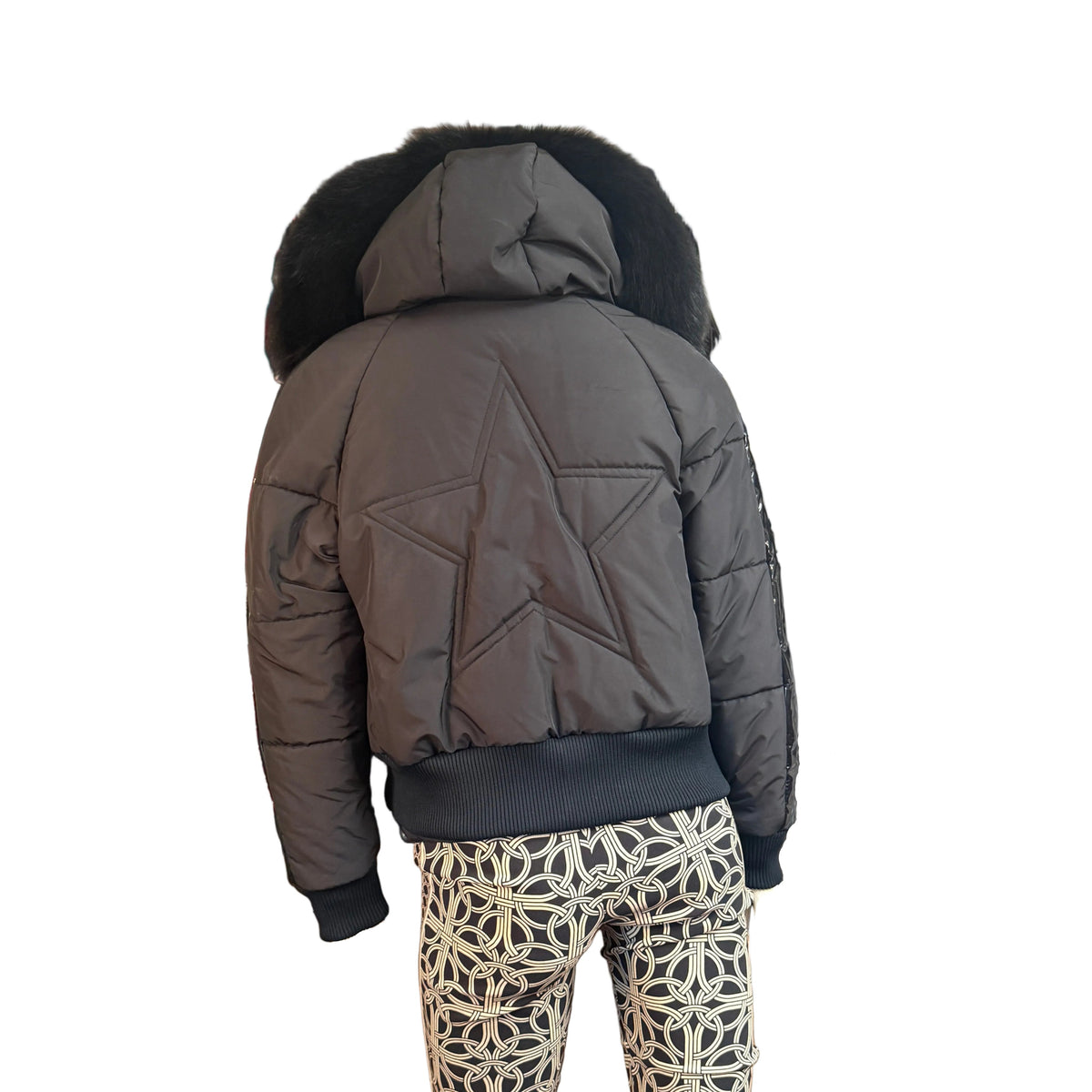 A black puffer jacket with a black fur-trimmed hood, shown from the back on a model wearing patterned pants against a white background.