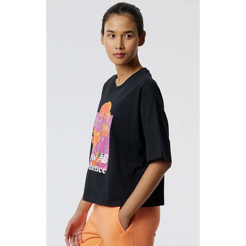 Women's New Balance Essential Bloom Tee. Black with floral pattern in the middle.  Side view.