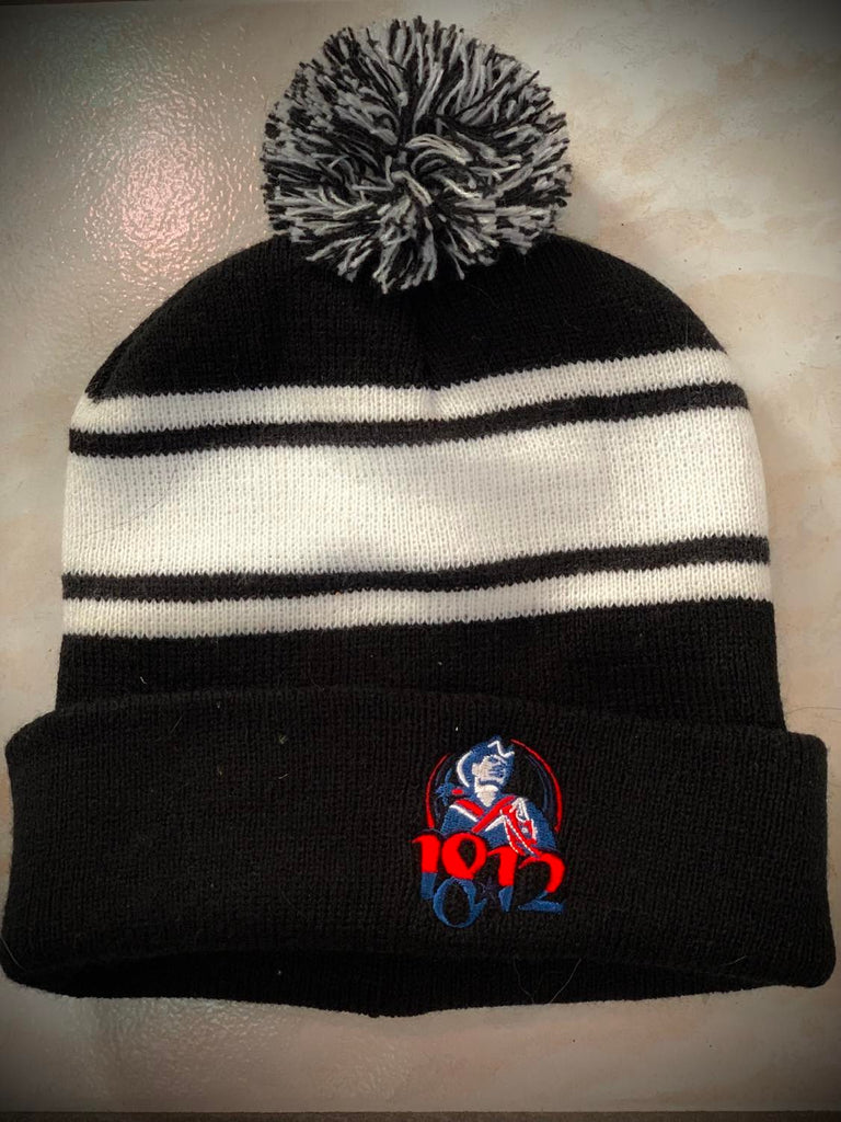 A black and white striped beanie with a pom-pom on the top and small 1812 red, white, and blue soldier logo.